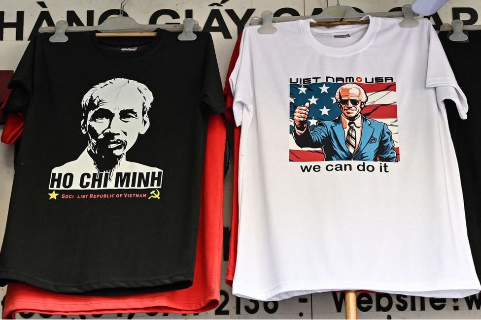 紀念品商店中，一名員工將一件印有美國總統拜登照片的T恤放在另一件印有越南已故國家主席胡志明肖像的T恤旁邊。
