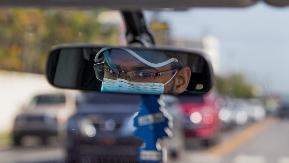 Водитель Uber носит маску, как видно в его зеркале заднего вида