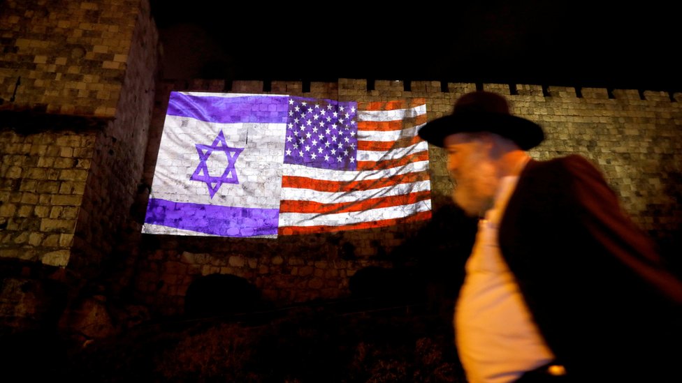 Un hombre camina junto a una proyección de las banderas de Estados Unidos y de Israel sobre el muro de la ciudad antigua de Jerusalén.