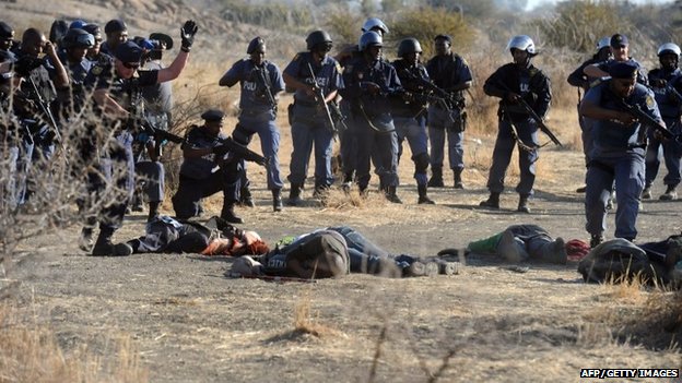 Полиция окружает упавших шахтеров после того, как они открыли огонь во время столкновений возле платинового рудника в Марикане.