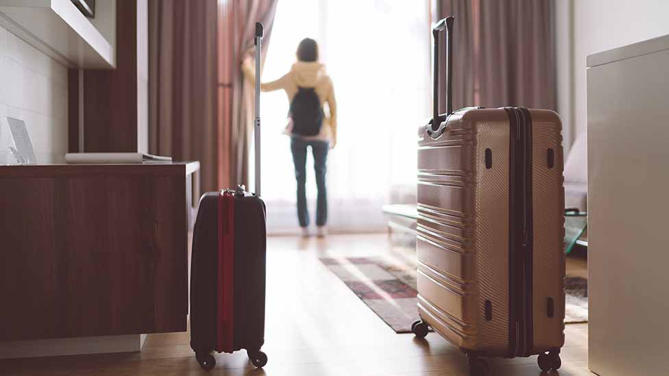 Woman with suitcases opens curtain in hotel room