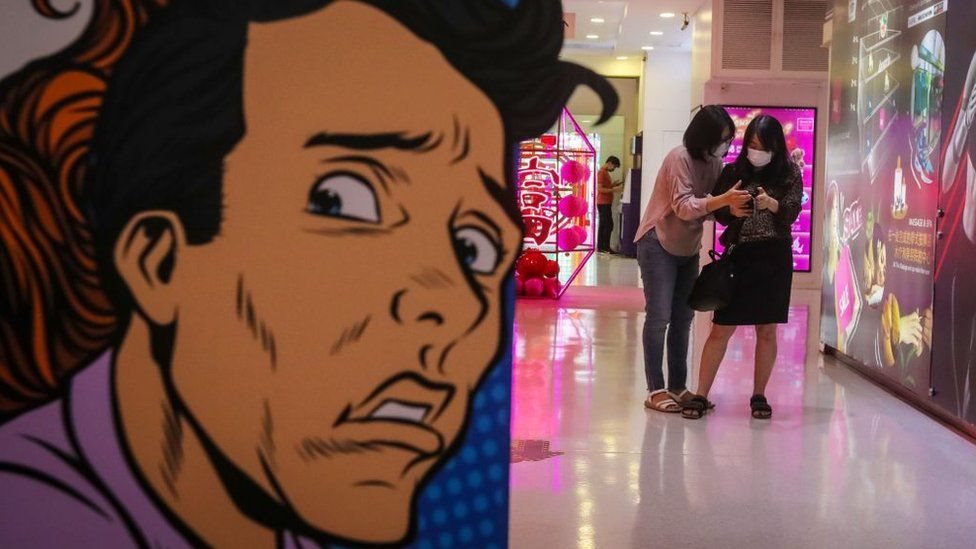 Dos jóvenes asiáticas con mascarilla y un mural de un hombre asustado.