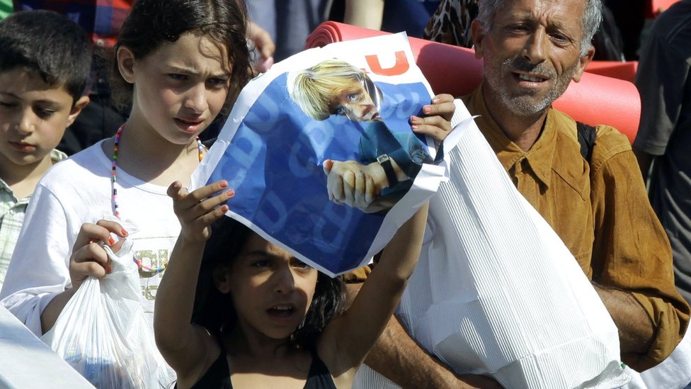 A migrant girl holds a poster of German Chancellor Angela Merkel as migrants walk in Budapest downtown after leaving the transit zone of the main train station, on September 4, 2015