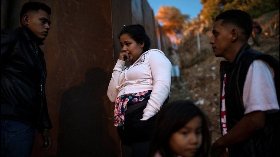 Migrantes de Honduras esperan enfrente de la valla