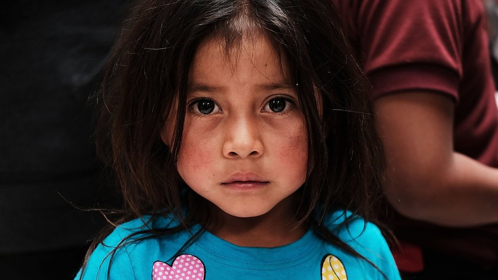 Una niña pequeña que migró junto a su familia mira fijamente a la cámara.