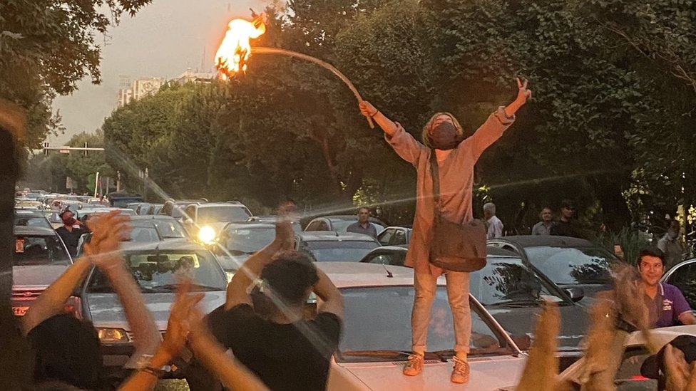 A woman stands on top of a car bonnet and sets her headscarf on fire on 19 September 2022 in central Tehran during protests for Mahsa Amini