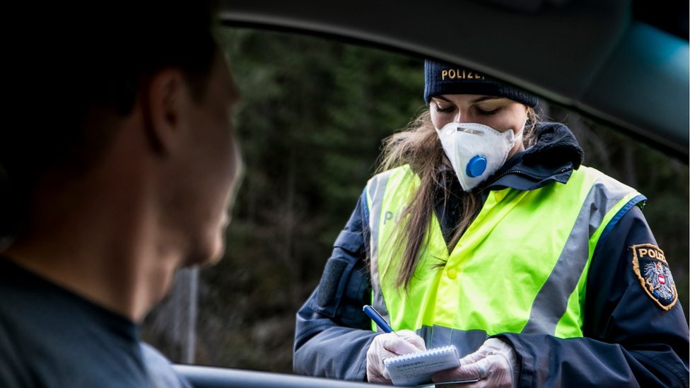 Полицейский на блокпосту спрашивает водителя автомобиля, выезжающего из долины Панцнауталь для проезда по разрешению после введения карантина из-за коронавируса 14 марта 2020 года недалеко от Ишгля, Австрия