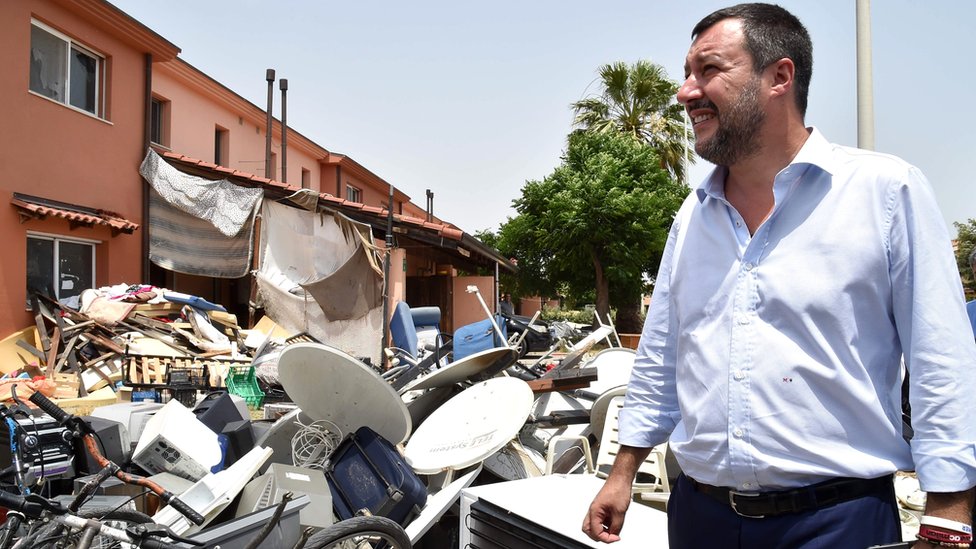 Маттео Сальвини стоит рядом с грудой мусора во время посещения центра мигрантов Минео, 9 июля 2019 г.