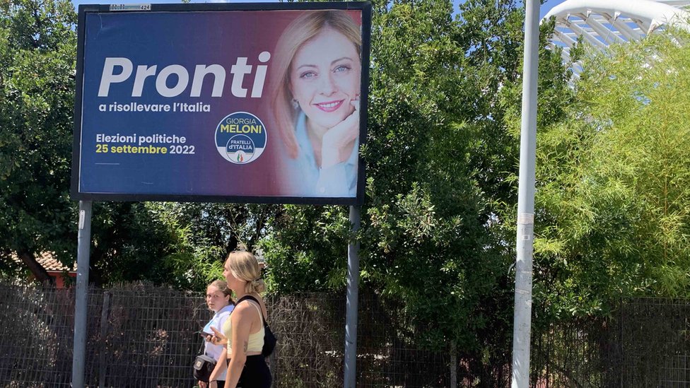 Women walk passed a 'Meloni' campaign sign in Garbatella