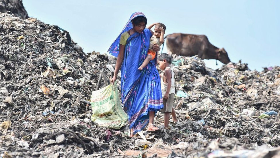 Una mujer de India carga a su bebé en brazos en un basurero.