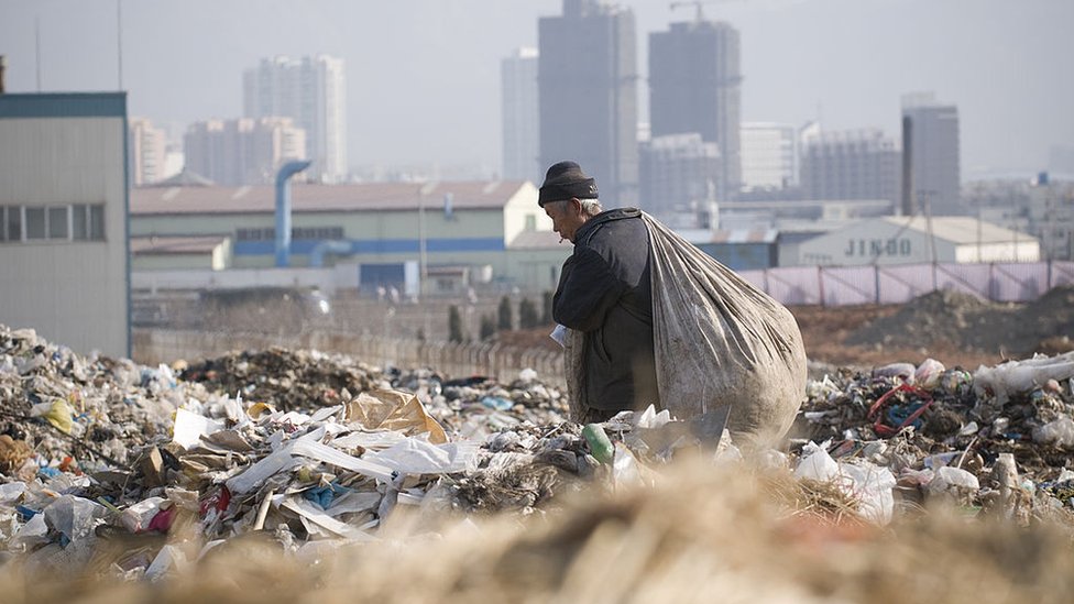 An elderly male migrant worker carries a large bag of plastic bottles he had collected at the Dalian Jinzhou garbage dump.
