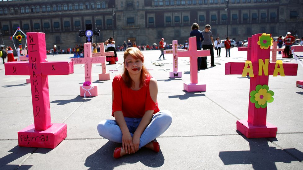 Женщина сидит среди розовых крестов во время акции протеста «День без женщин» в Мексике