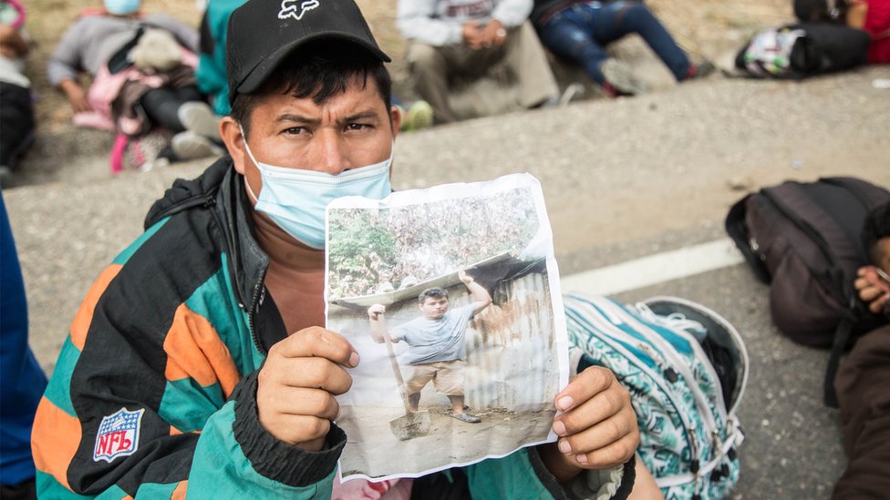 Wilmer, un hondureño de la caravana de migrantes que cruza Guatemala, muestra una foto de su casa destruida por la tormenta Eta, razón por la cual decidió emprender el éxodo de Honduras, mientras descansaba con otros migrantes en Chiquimula, Guatemala.