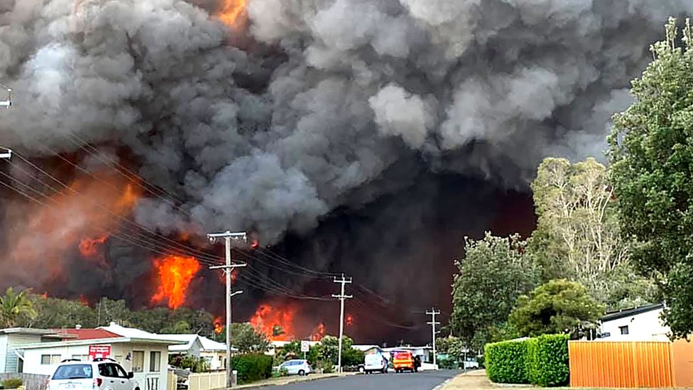 Огромные облака пламени и дыма от крупного лесного пожара нависают над пригородной улицей Харрингтона, Новый Южный Уэльс