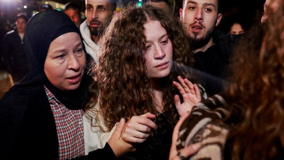 Ahed Tamimi com olhar sério ao lado da mãe e rodeada por outras pessoas