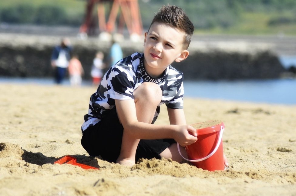 Мальчик наполняет пластиковое ведро песком на пляже
