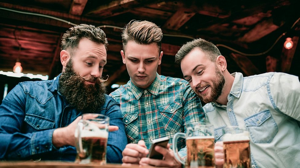 Three men in a bar looking at a mobile phone