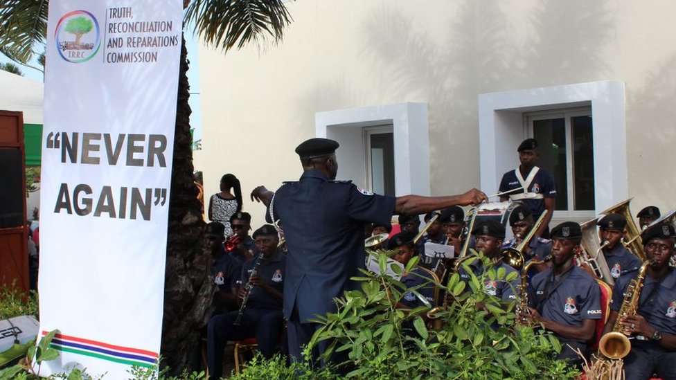A band playing at the launch of the TRRC next to a banner saying, "Never again" - October 2018