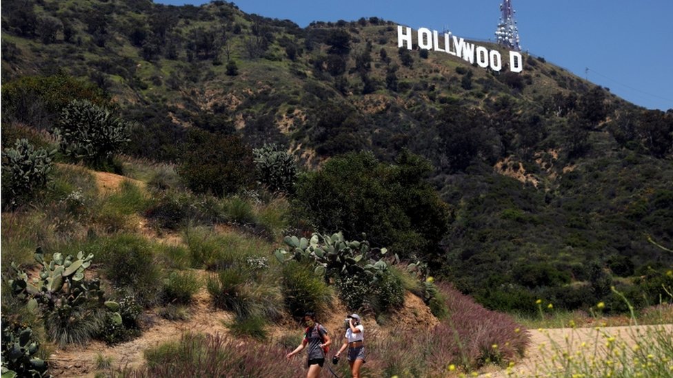 Люди идут пешком под знаком Голливуда после того, как пешеходные тропы в Лос-Анджелесе частично открылись во время вспышки коронавирусной болезни