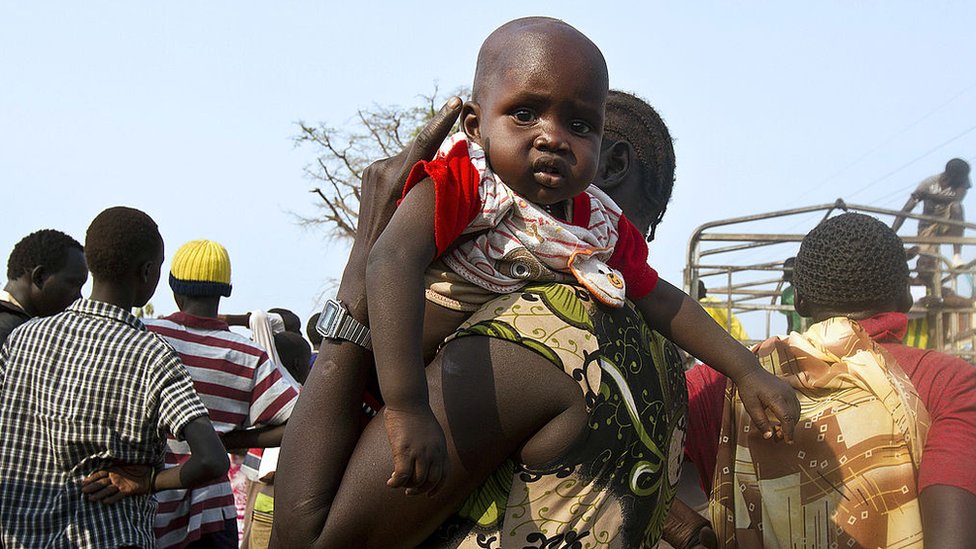 أمرأة تحمل رضيعاً بينما ينتظر اللاجئون من جنوب السودان عربات لتنقلهم من مركز اللاجئين في شمالي أوغندا إلى معسكر خاص للاجئين