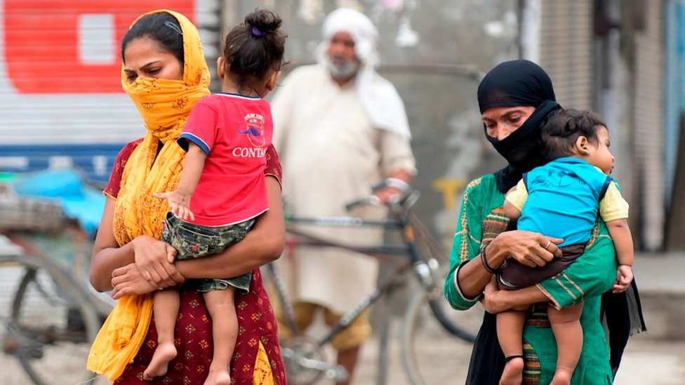 Женщины в масках несут и своих детей гуляют по окраине Амритсара 5 сентября 2020 года.
