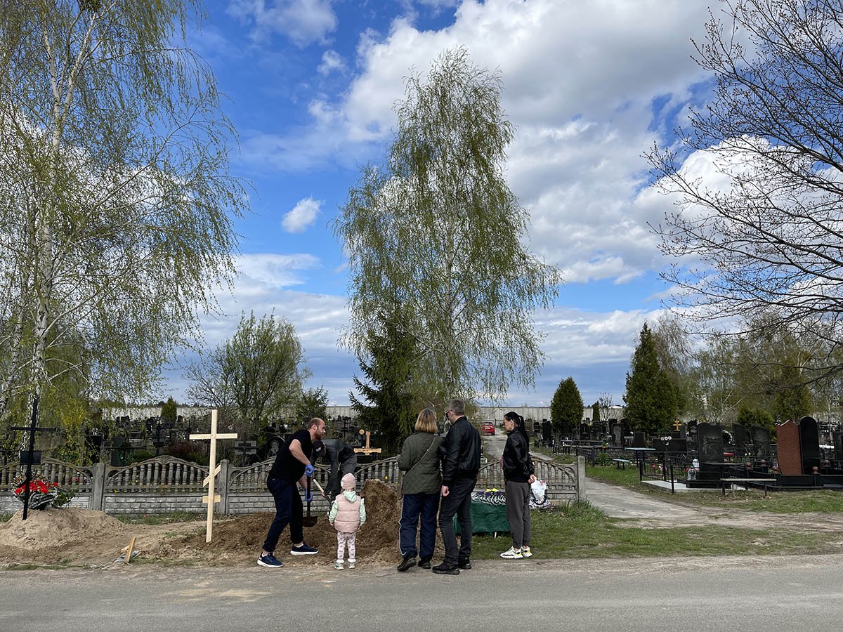 family in Bucha cemetery - a fresh grave is being dug