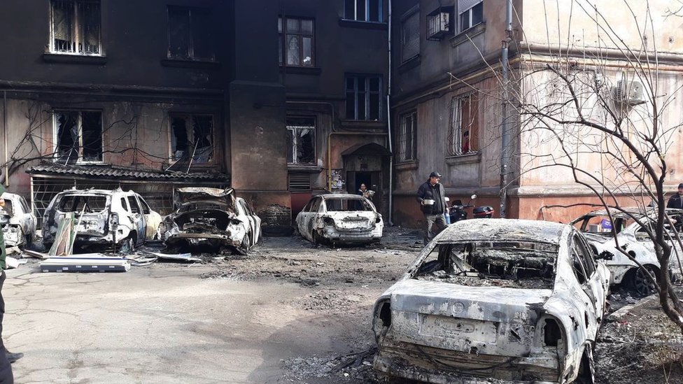 Cars destroyed by fire parked in front of a charred building in Mariupol