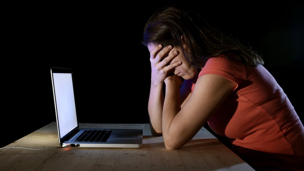 En la mayoría de los casos, los niños afectados no lo cuentan. niña usando computadora y cubriéndose la cara.