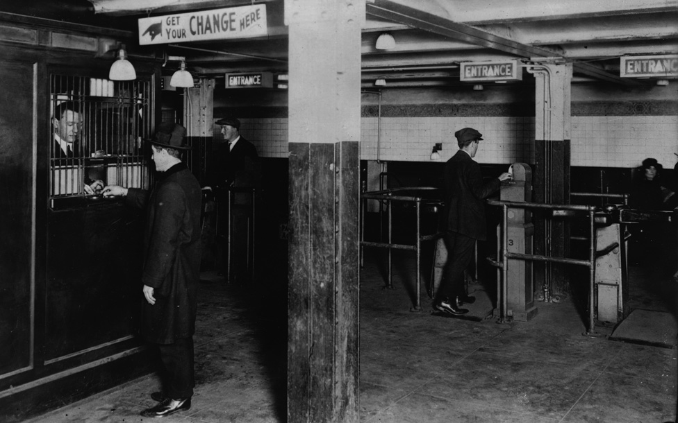 Мужчина получает сдачу, чтобы пройти через билетный барьер в метро Нью-Йорка в 1920-е годы