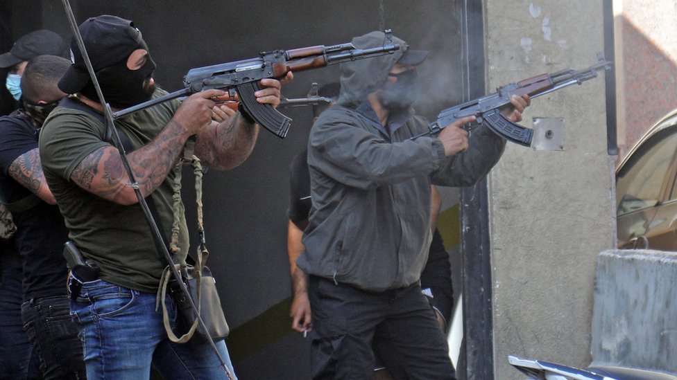 Shia fighters from Hezbollah and Amal movements take aim with Kalashnikov assault rifles amidst clashes in the area of Tayouneh, in the southern suburb of the capital Beirut, on October 14, 2021
