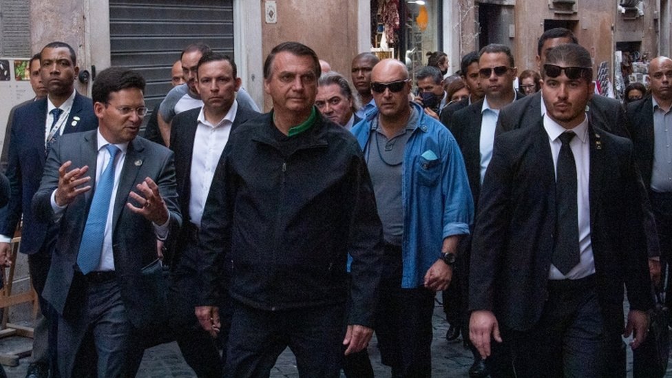 Bolsonaro caminha na rua rodeado de assessores e seguranças