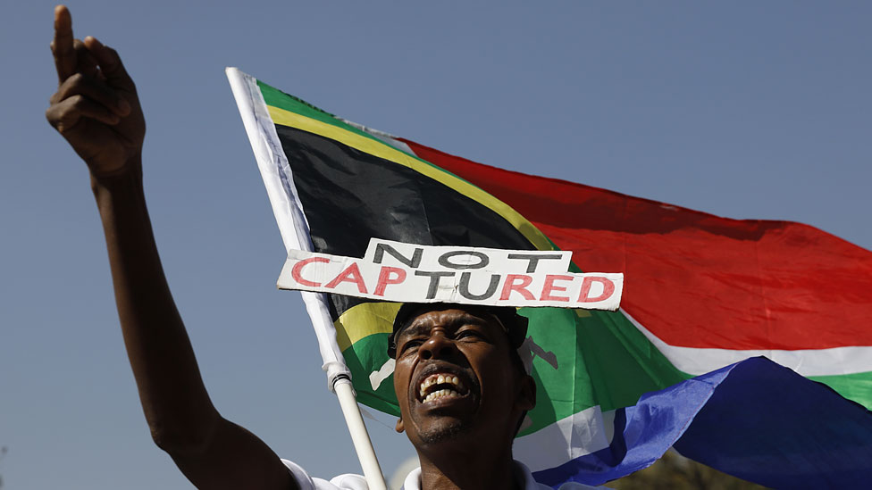 Сторонник Организации по борьбе с налоговыми злоупотреблениями (Outa) держит флаг Южной Африки во время пикетирования перед судебной комиссией по расследованию дела Раймонда Зондоса в Парктауне 20 августа 2018 года в Йоханнесбурге, Южная Африка.