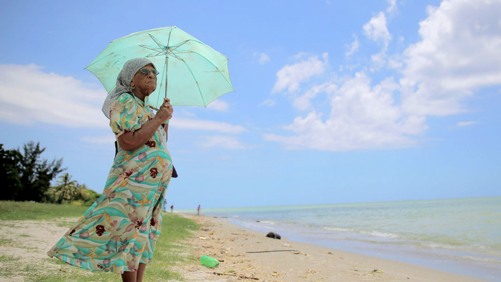Señora chagosiana frente al mar mirando al horizonte con una sombrilla para protegerse del sol