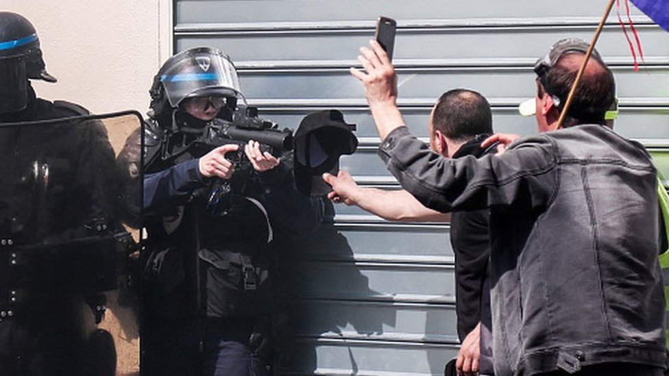 Policía apuntando con una pistola de balas de goma a un manisfestante