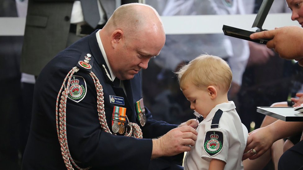 Сельская пожарная служба Нового Южного Уэльса (NSW RFS) показывает комиссара RFS Шейна Фицсиммонса (слева), прикрепляющего медаль к Харви Китону