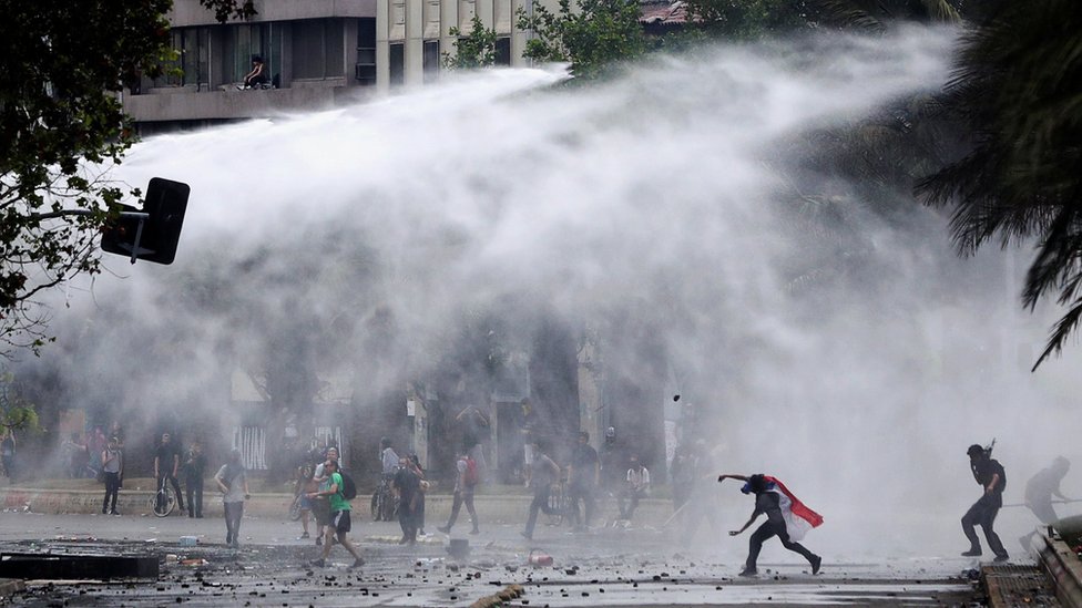 ОМОН стреляет из водометов во время столкновения с демонстрантами во время акции протеста против экономической модели Чили в Сантьяго