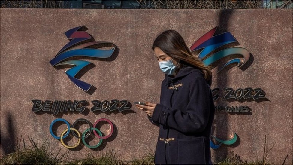 A woman wearing a face mask walks past the 2022 Beijing Winter Olympic and Paralympic emblems next to the headquarters of the 2022 Beijing Winter Olympics organising committee, at the Shougang Industrial Park, which will be used as a venue for hosting sport and other events during Beijing 2022 Winter Olympics, in Beijing, China, 01 December 2021