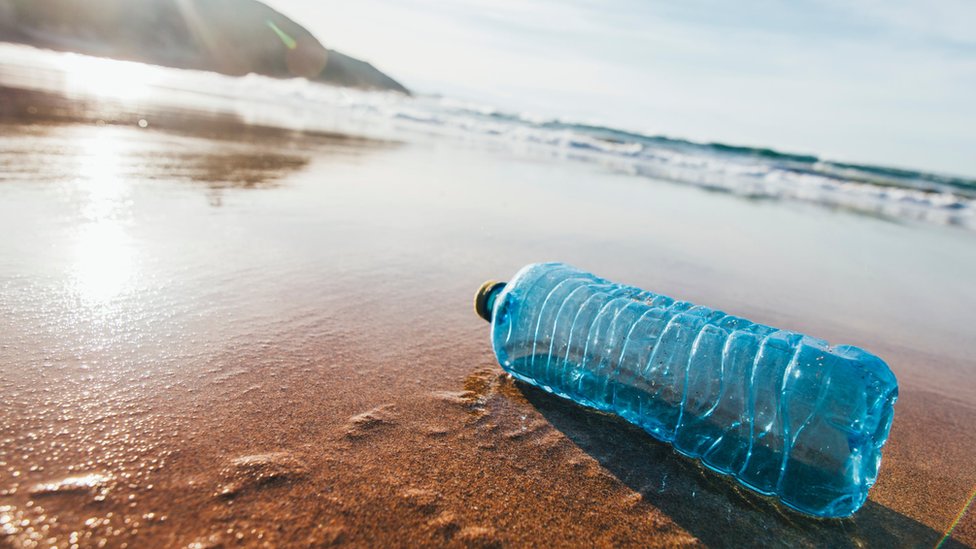 Одна выброшенная пластиковая бутылка с водой на песчаном пляже