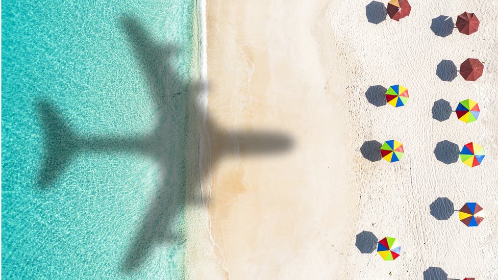 Sombra de avión sobre playa con parasoles en una isla del Caribe.