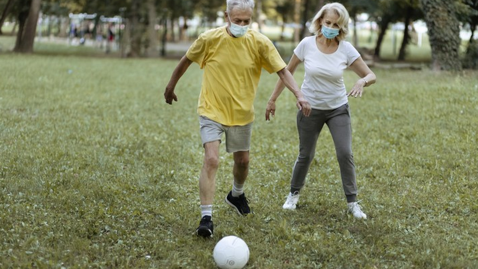 Homem e mulher de máscara jogam futebol