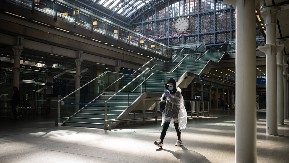 Женщина в защитной маске и пластиковом чехле от дождя ожидает, когда поезд отправится на посадку на международном вокзале Сент-Панкрас 4 мая 2020 года в Лондоне, Англия