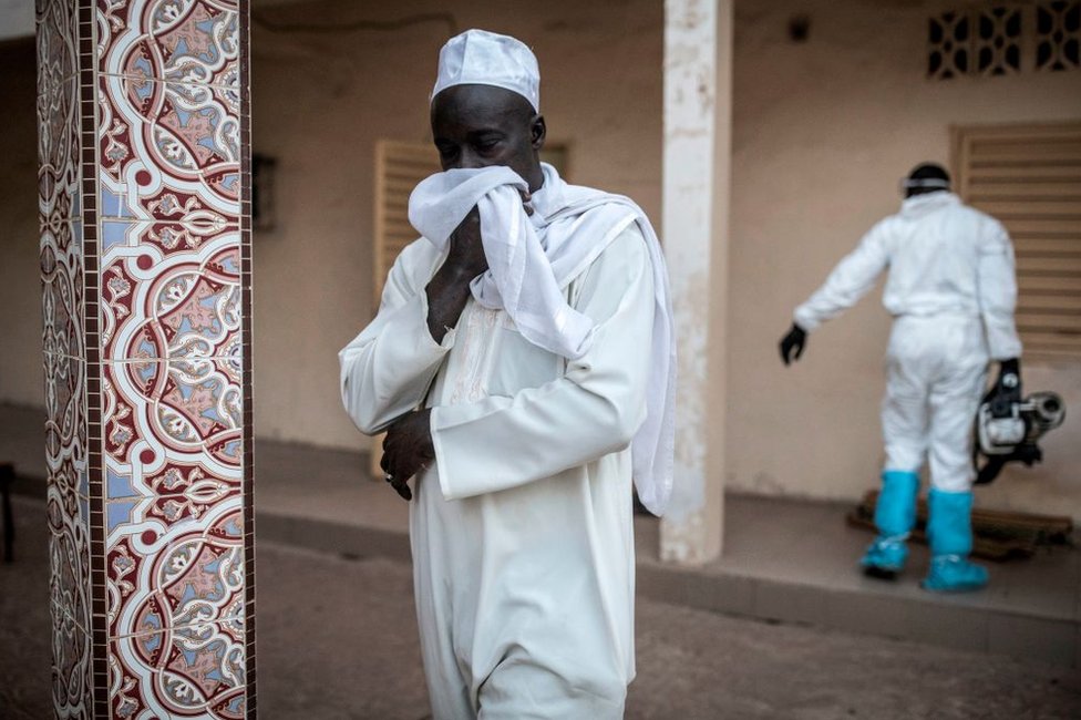 Un hombre se tapa la boca con un pañuelo mientras otro desinfecta una mezquita en Dakar, Senegal, como medida preventiva contra el coronavirus, el 1 de abril de 2020.