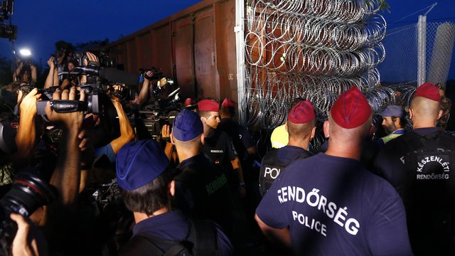 Hungarian police officers guard the area as a rail wagon prepared with barbwire arrives to seal the border fence between Serbia and Hungary in Roszke