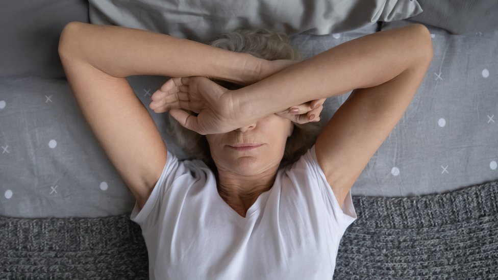 Una mujer en la cama con dificultades para dormir se cubre los ojos con los brazos