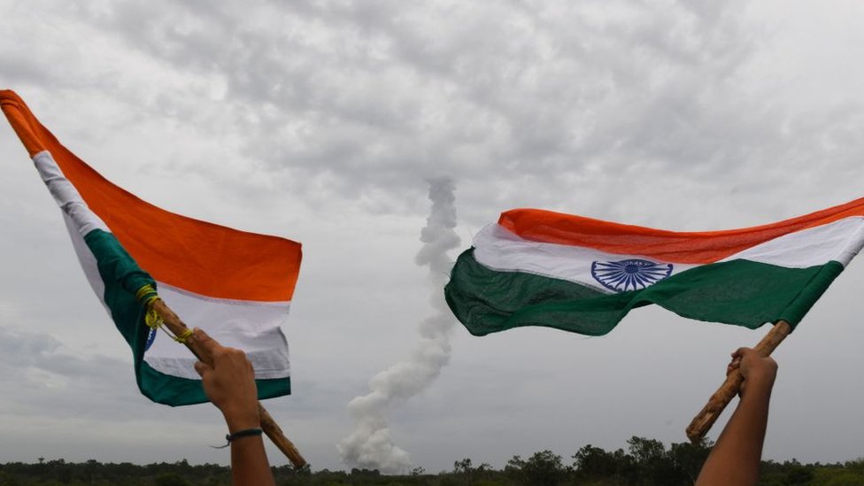 Жители Индии размахивают национальными флагами Индии, когда Индийская организация космических исследований (ISRO) Chandrayaan-2 (Moon Chariot 2) на борту геосинхронной ракеты-носителя (GSLV-mark III-M1) запускается в Шрихарикоте в штате Андхра-Прадеш. 22 июля 2019 г.