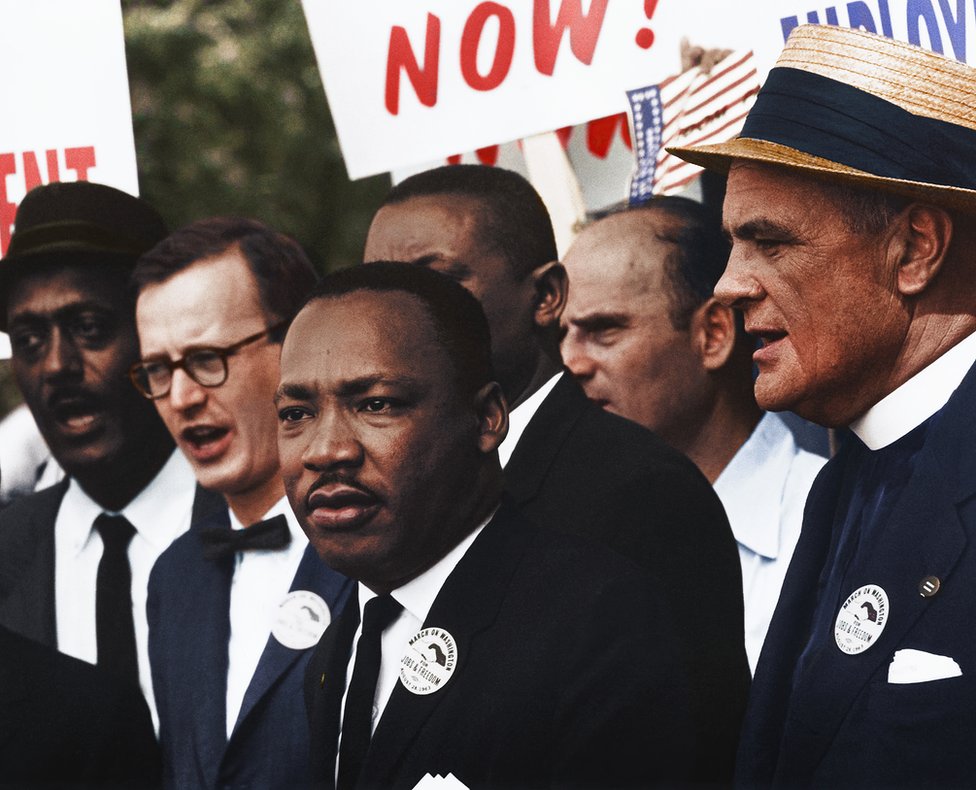 Доктор Мартин Лютер Кинг стоит с другими на марше на цветной фотографии