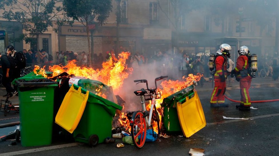 Пожарные стоят возле мусорных баков, мусора и горящего велосипеда на улицах Парижа