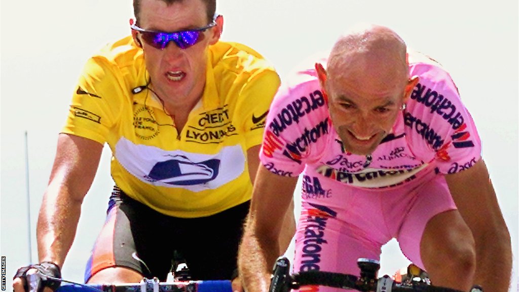 Marco Pantani rides ahead of Lance Armstong, in the yellow jersey, grimacing over his handlebars.