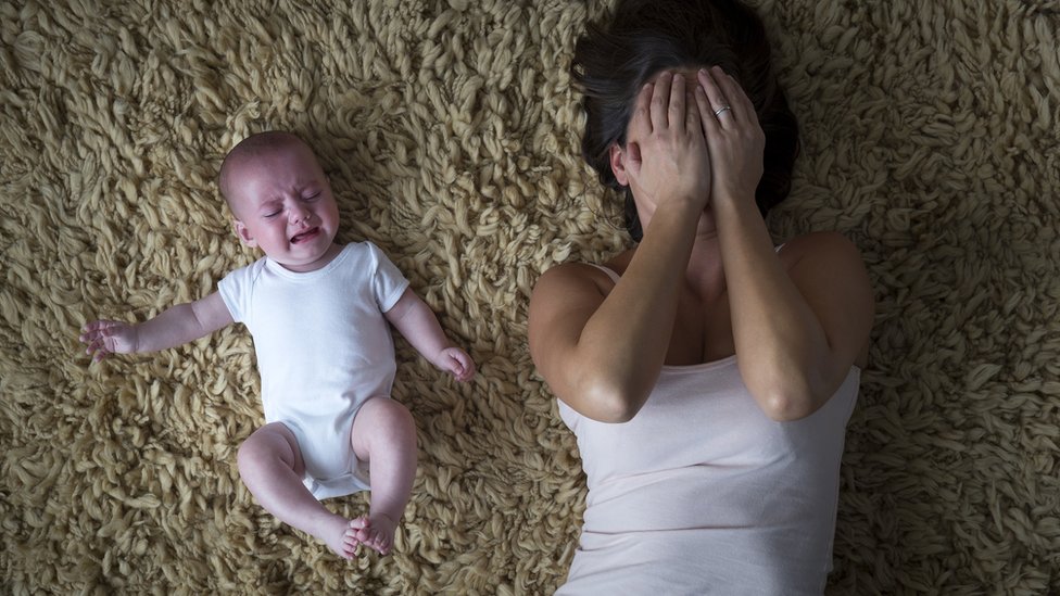 Madre se cubre el rostro mientras su bebé llora a su lado