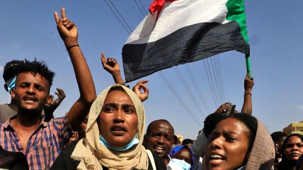 Sudanese protesters flash victory signs and lift national flags as they demonstrate on 60th Street in the capital Khartoum, to denounce overnight detentions by the army of government members, on October 25, 2021.